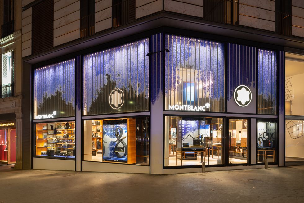 Exterior de botiga Montblanc de nit amb finestres il·luminades mostrant productes i disseny artístic blau.