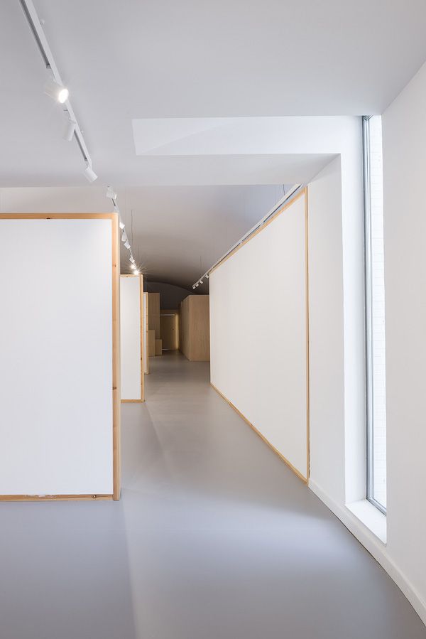 Passadís amb disseny minimalista, amb parets blanques, marcs de fusta i una gran finestra a la dreta.