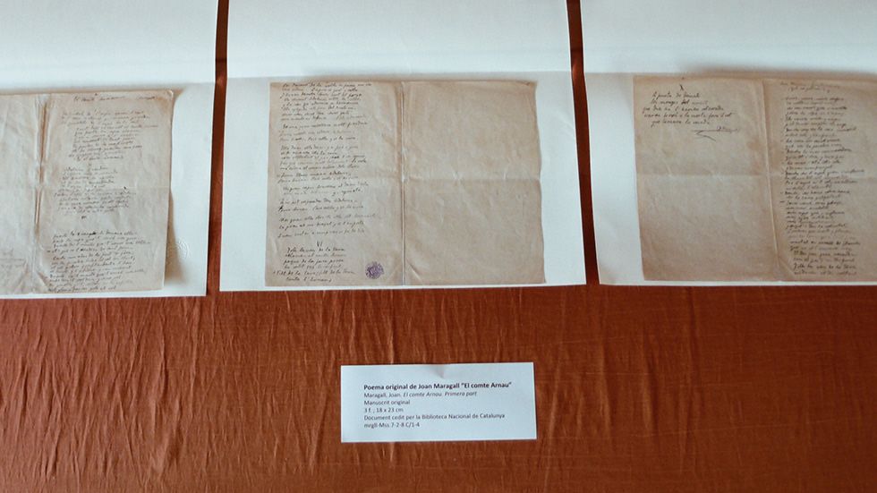 Manuscrits originals de poemes del segle XIX exposats sobre un teixit taronja.
