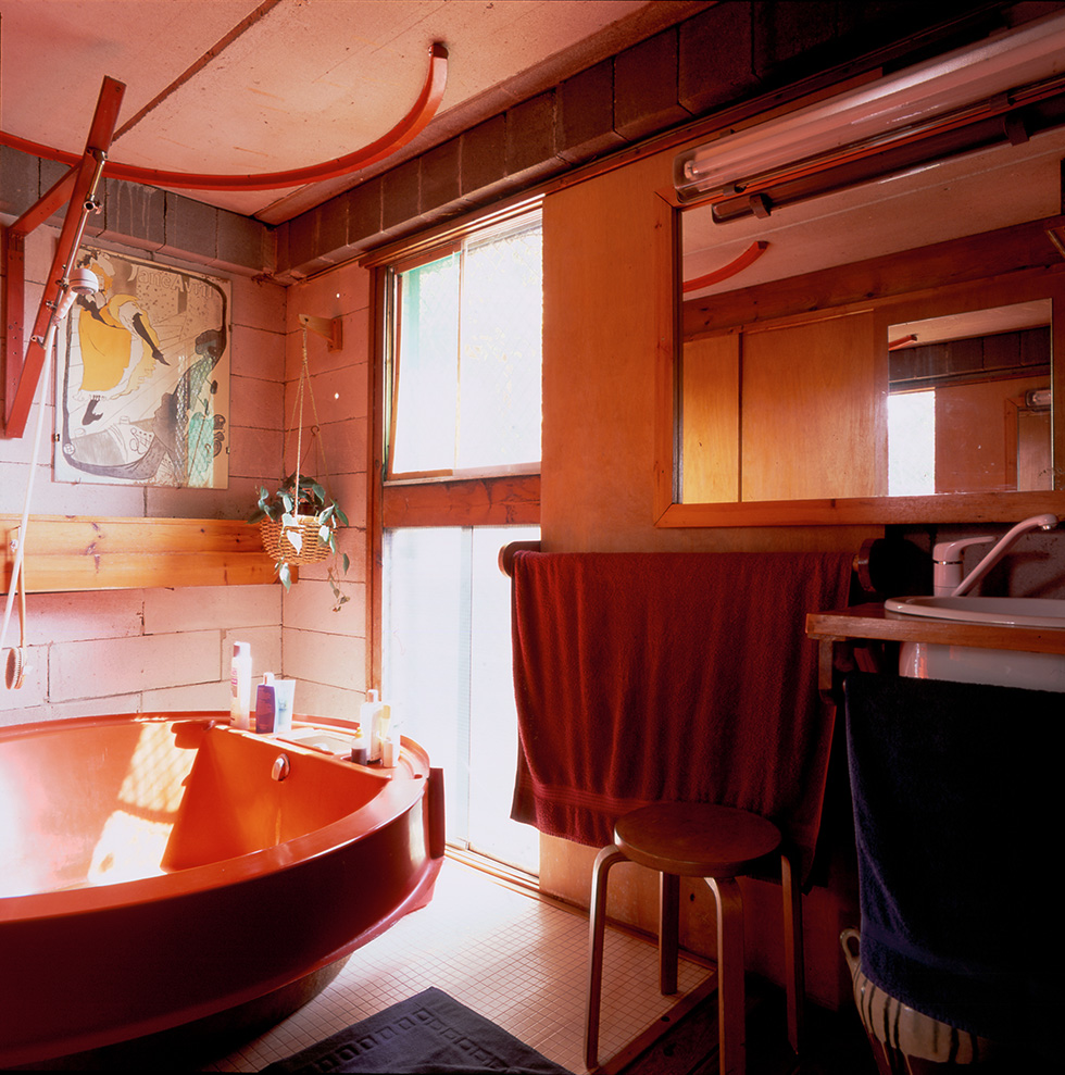 Bathroom with a red bathtub, wooden elements, a floor-to-ceiling window, and a variety of towels hanging below a mirror and a bathroom sink.