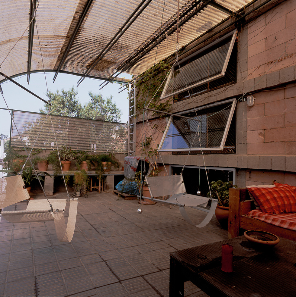 Terraced outdoor area with a translucent arched roof, hanging swings, potted plants, and open horizontal pivoting windows.