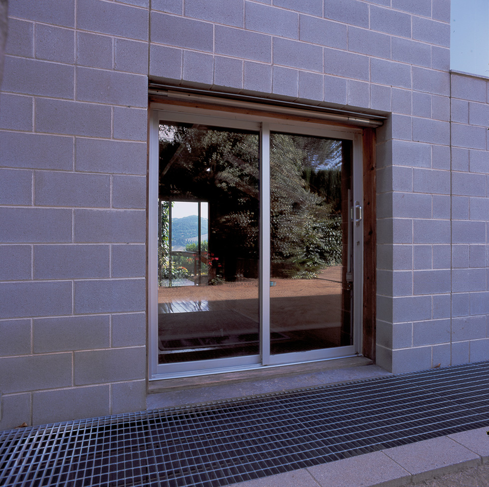 Sliding glass door on a concrete block wall, reflecting the outdoor greenery and a distant view of the hills.