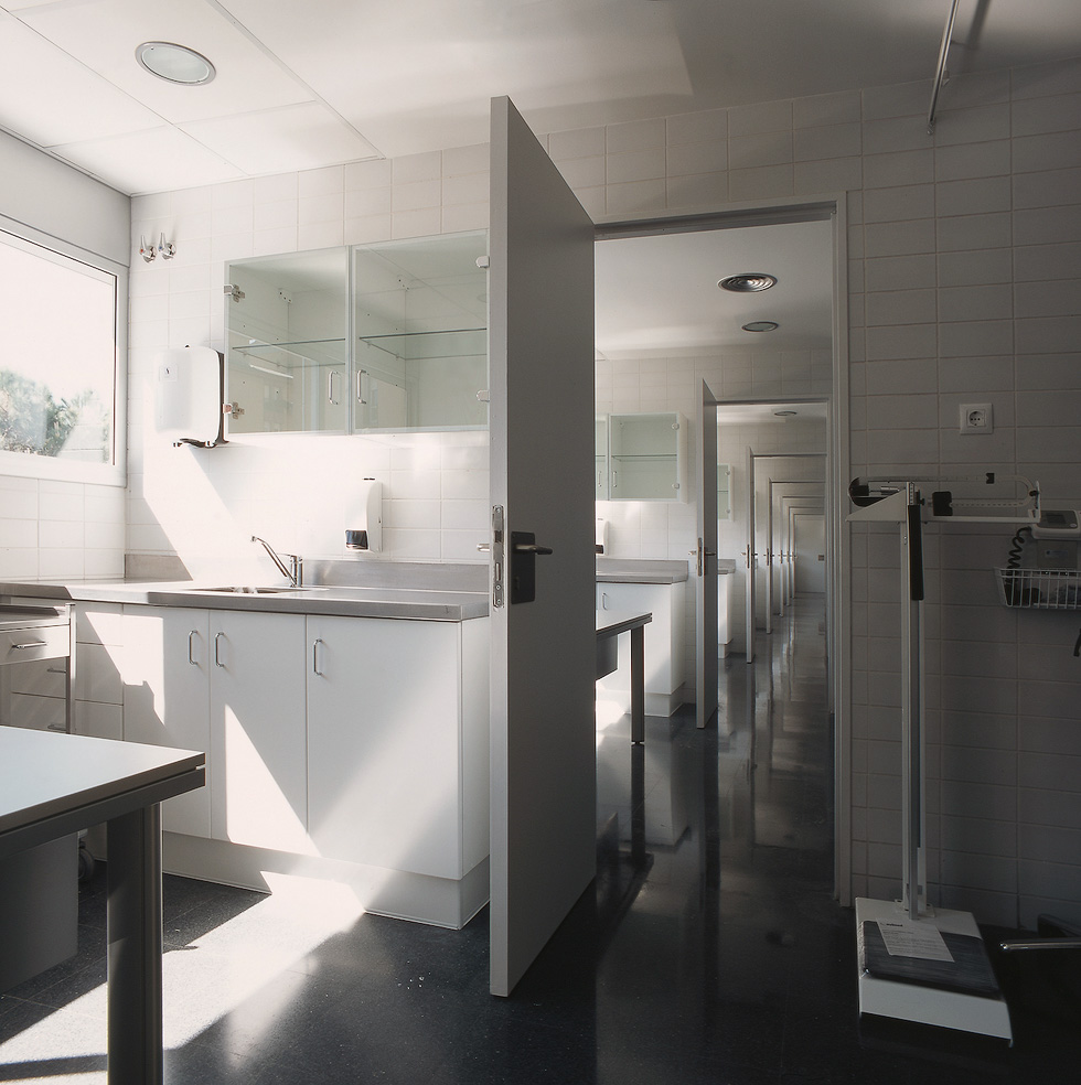 A modern medical clinic hallway with clean, white cabinetry and multiple open doors, reflecting a bright and clean environment.