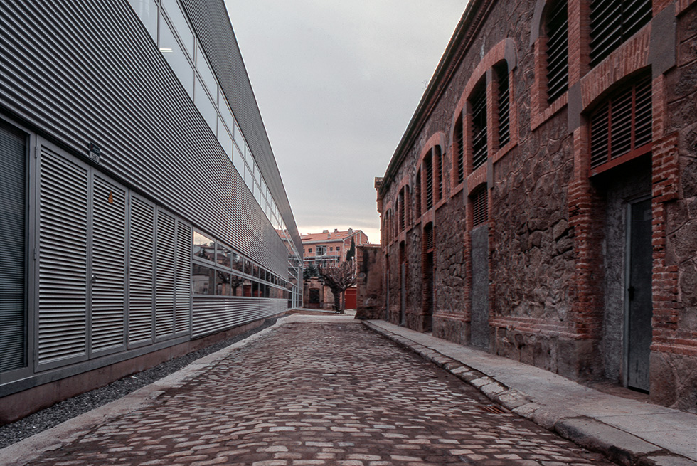 A cobblestone street between a modern building with metal siding and an old brick building with arched windows.