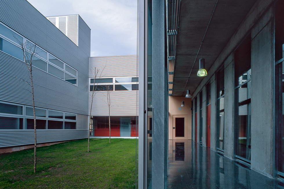 Modern building courtyard with metallic facade, glass windows, and green lawn area.