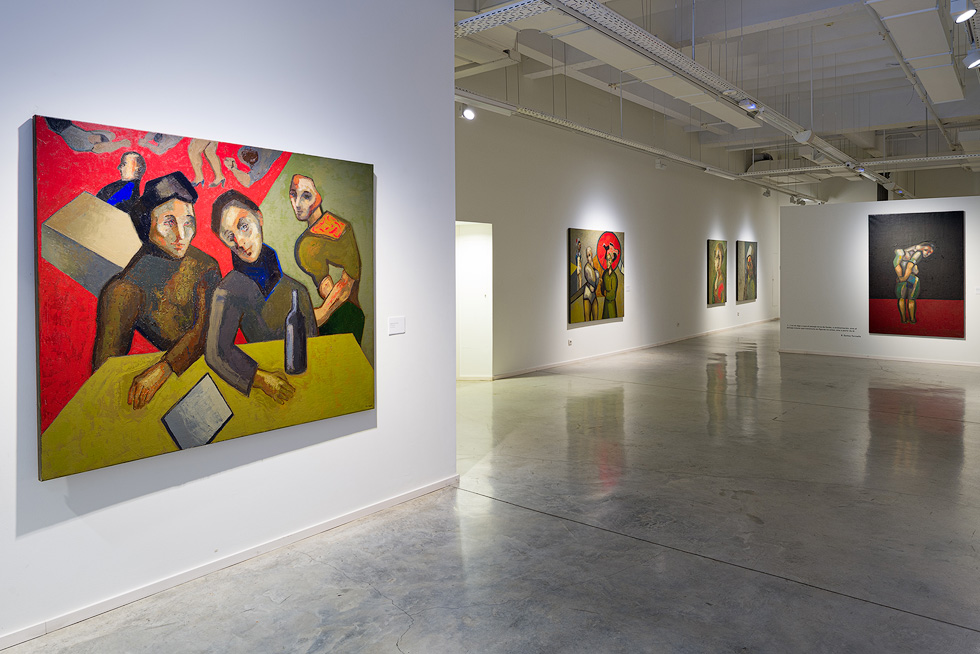 Large exhibition space featuring colorful paintings by Guerrero Medina, including a prominent piece depicting three figures at a table.