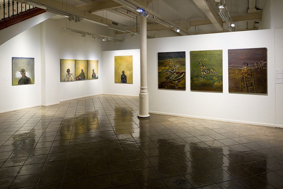 A gallery corner featuring a series of paintings with abstract and figurative elements on white walls.