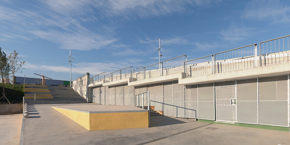 A concrete and metal structure in a park with a staircase, railings, and yellow accents, under a clear blue sky.