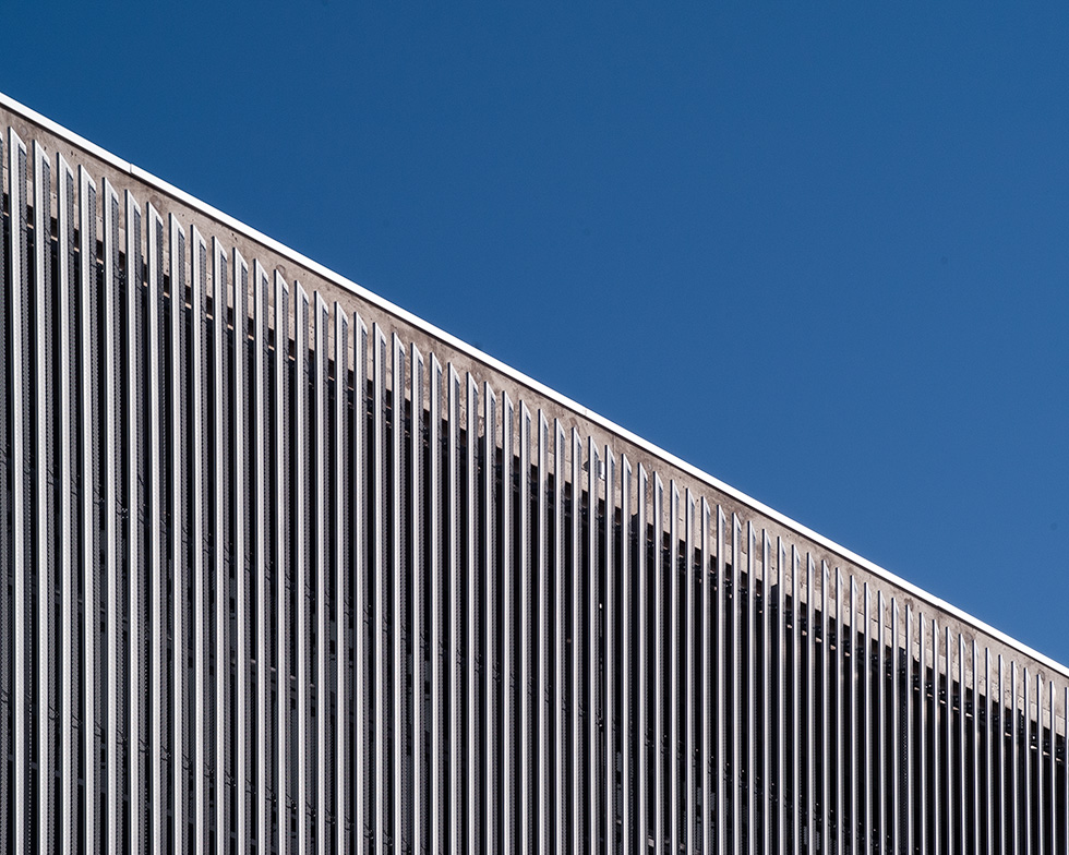 Angled view of Artes High School's facade showcasing the vertical metal slats against a clear blue sky, emphasizing the modern architectural design.