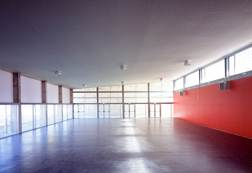 Interior of the gymnasium, featuring a spacious open floor with large windows and a vibrant red accent wall.