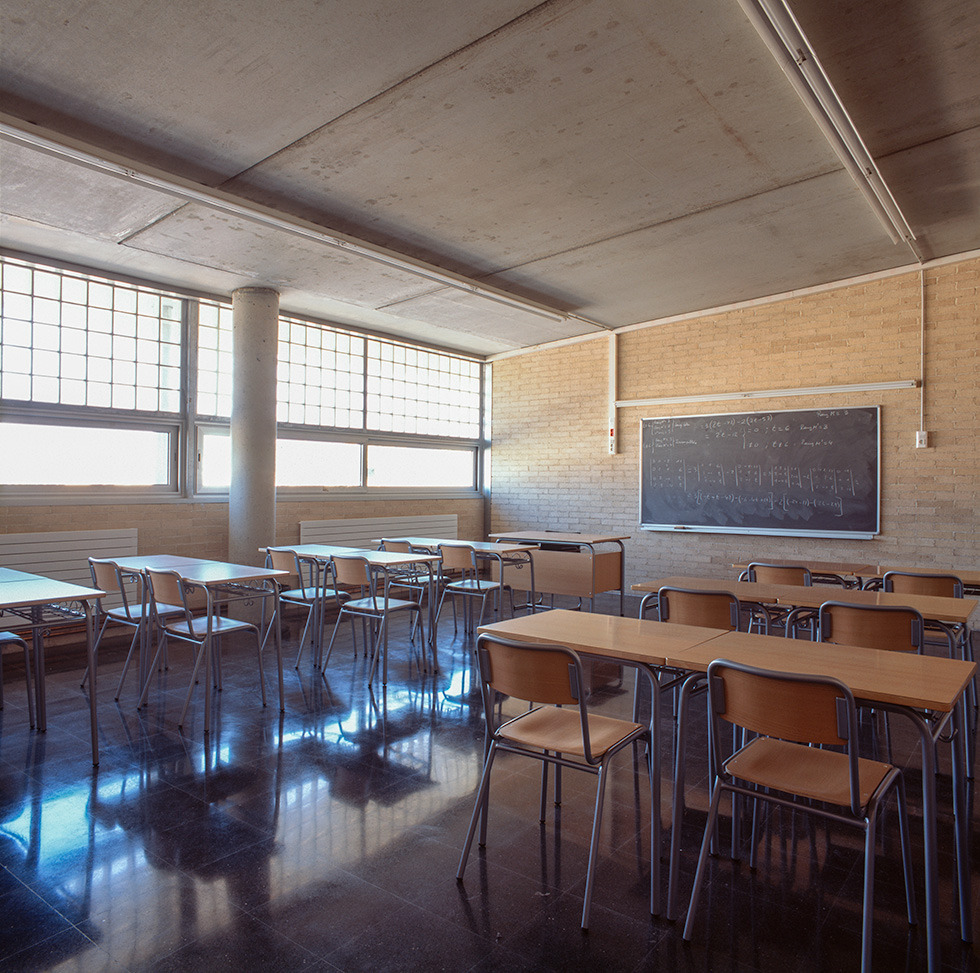 Classroom with wooden desks and chairs, a large blackboard, and windows allowing natural light to illuminate the space.