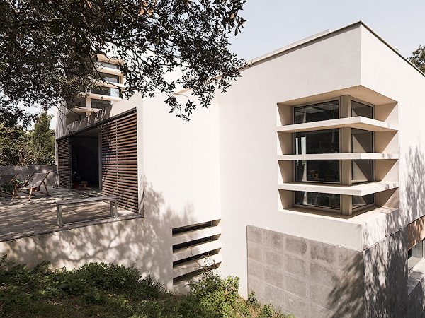 Modern house exterior with large windows and a spacious terrace, surrounded by trees and natural landscape.