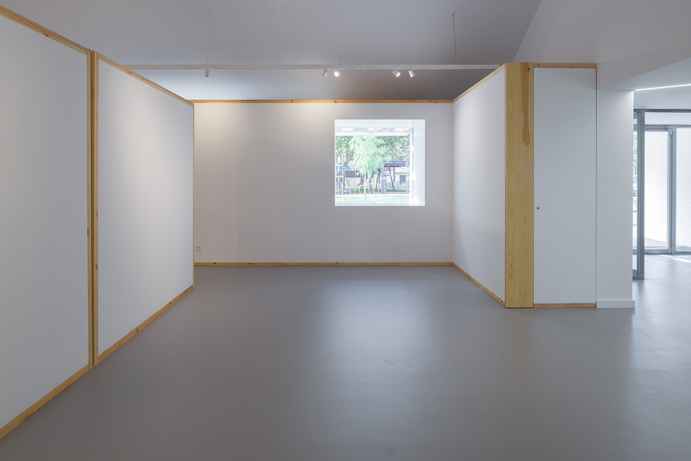 Minimalistic interior with white walls and wooden frames, featuring a single window providing a view of the outdoors.