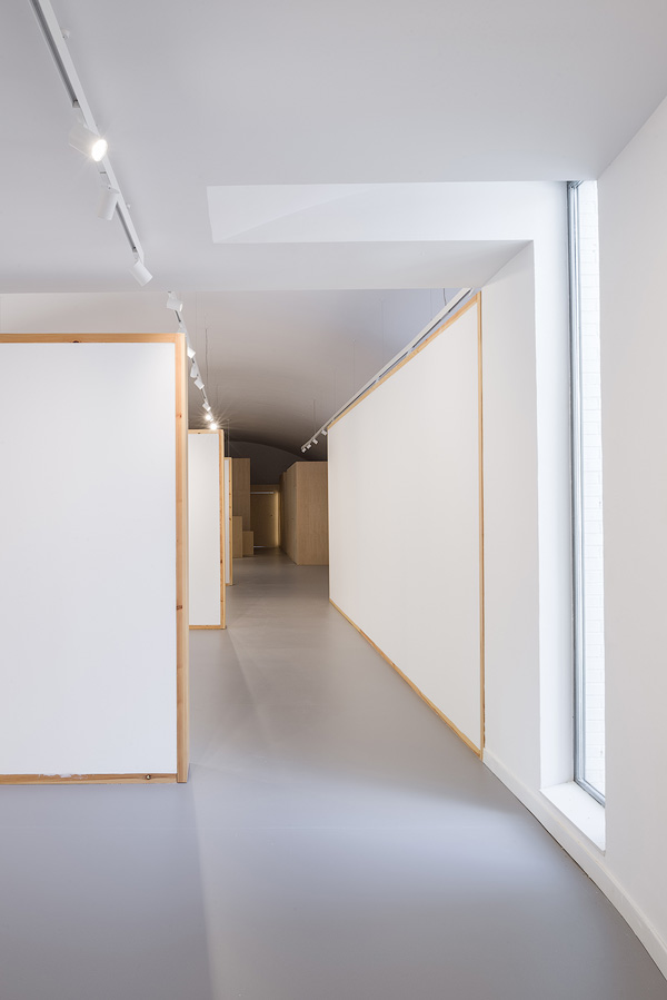 Hallway with minimalist design, featuring white walls, wooden frames, and a large window on the right.