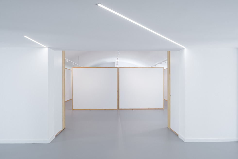 Minimalist interior with white walls and geometric panels, illuminated by sleek linear lighting.