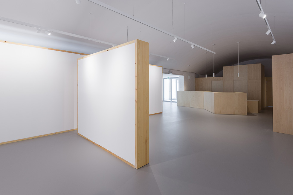 Interior space with white partition walls and wooden accents, leading to a reception area with wooden counters and pendant lights.