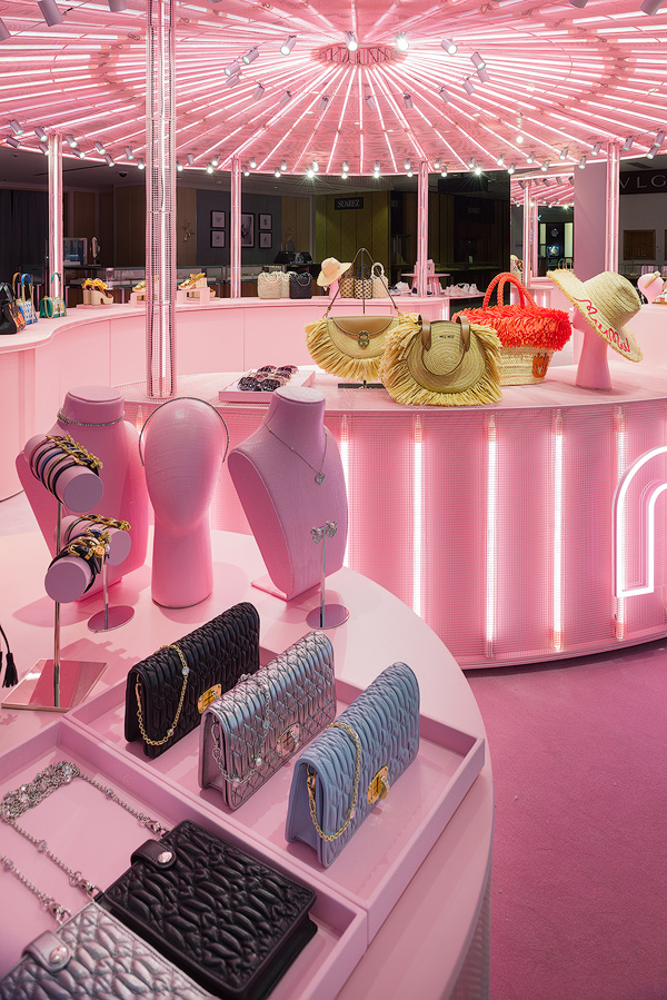 Display of Miu Miu handbags, jewelry, and hats in a brightly lit pink pop-up store.