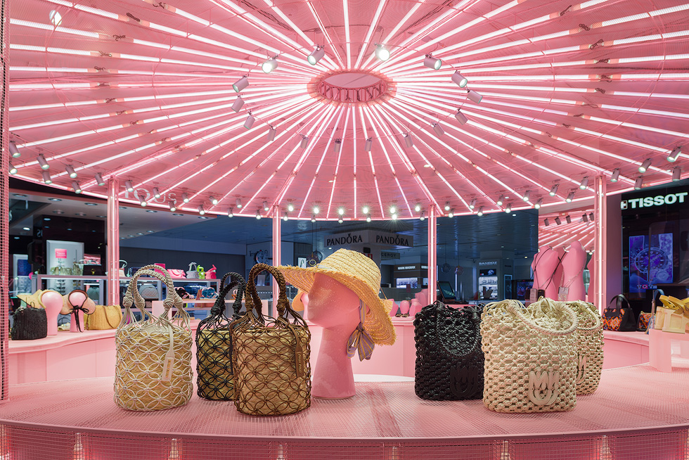 Woven bags and hats displayed under pink illuminated ceiling in Miu Miu's pop-up store.