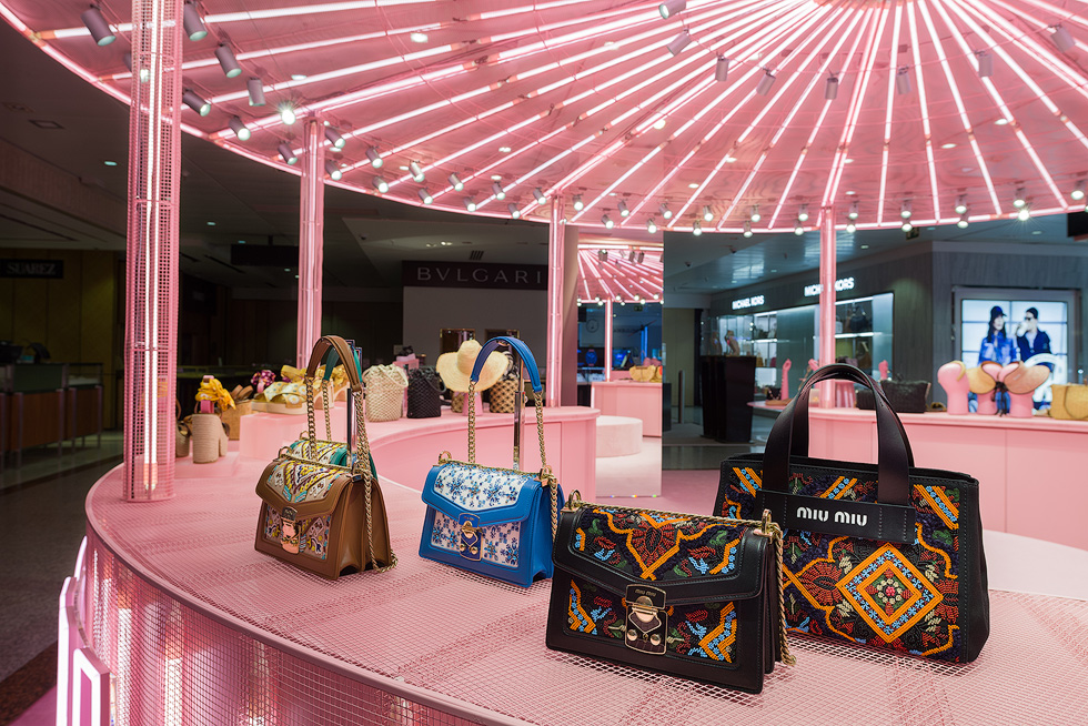 Embroidered handbags on display under pink illuminated ceiling in Miu Miu's pop-up store.