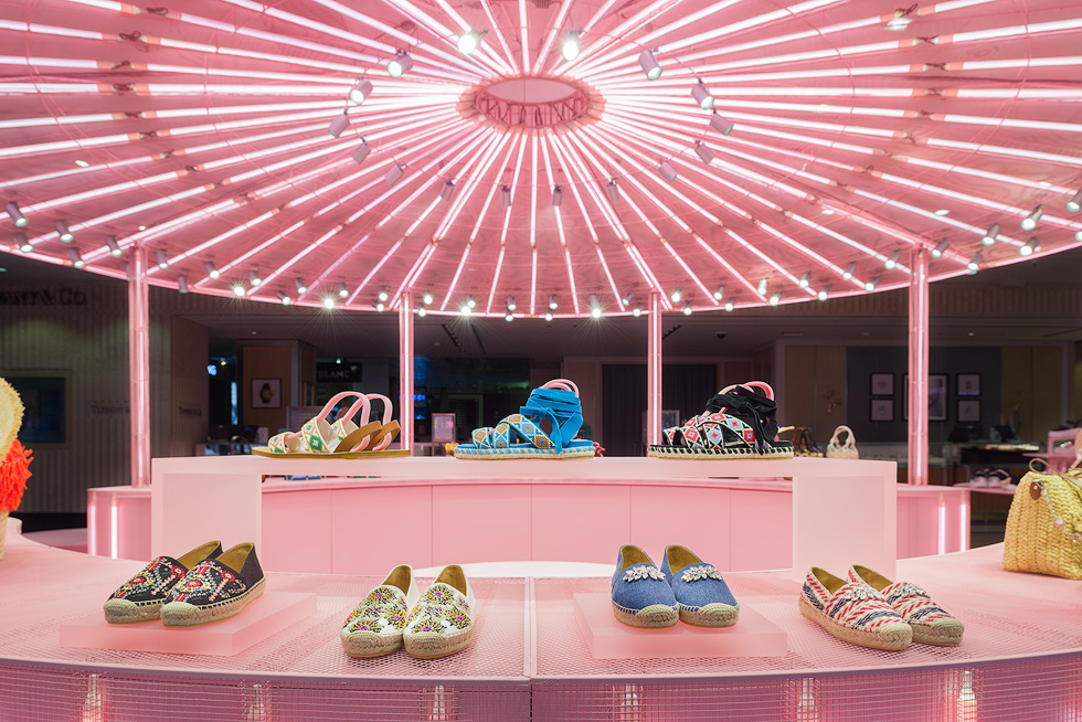 Brightly colored sandals and espadrilles displayed under a radiant pink canopy in Miu Miu's vibrant pop-up store.