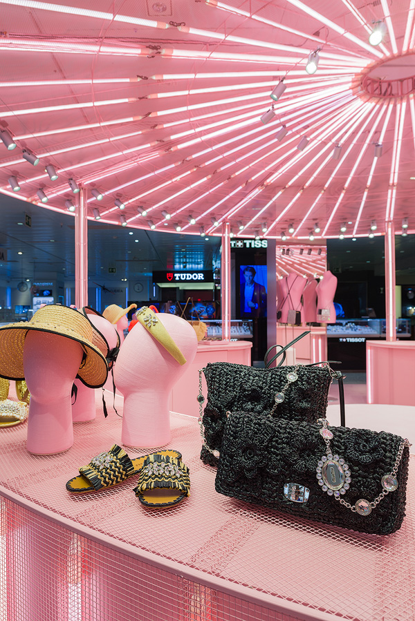 Hats and bags displayed on pink mannequin heads under vibrant pink lighting in Miu Miu's pop-up store.