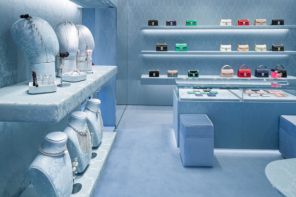 Jewelry and handbags displayed in a Miu Miu store with blue textured walls and shelves.