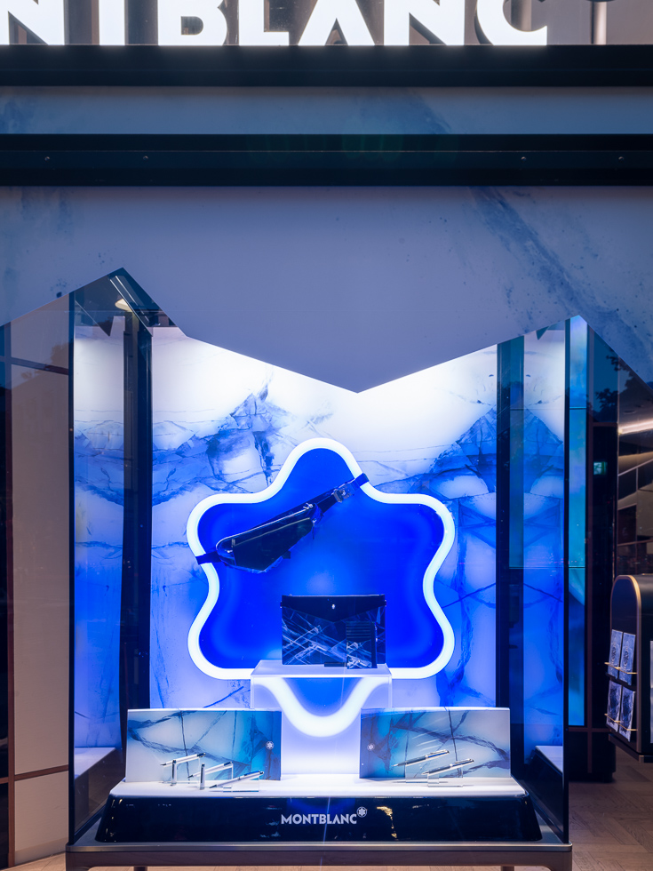 Montblanc store display with a blue glacier-themed backdrop showcasing bags and writing instruments.