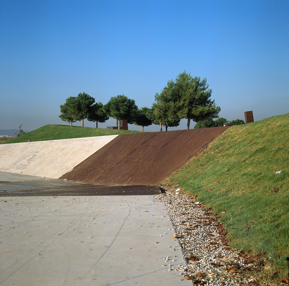 A sloped concrete and corten steel surface in a landscaped park area with trees in the background.