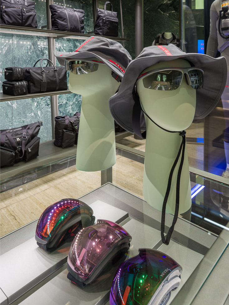 Luxury Prada boutique, a glass table displays eyewear, hats, and performance skiing eyewear.