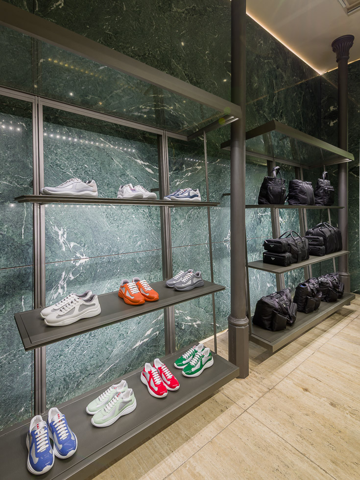 Luxury Prada boutique with green marble walls, showcasing designer sneakers and black bags on sleek metal shelving.