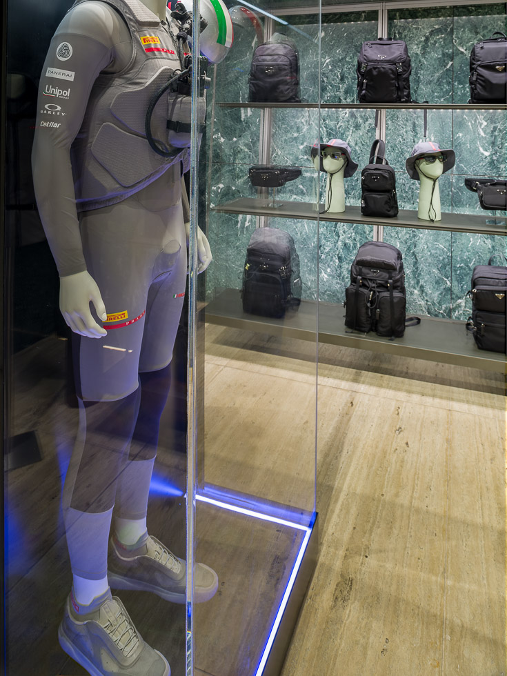 Luxury Prada boutique with green marble walls, showcasing a mannequin in a performance outfit encased in a glass display.