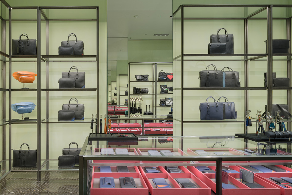 Prada store interior with two facing mirrors featuring an infinity mirror effect, there are shelves of designer bags in various colors, organized neatly against a light green background.