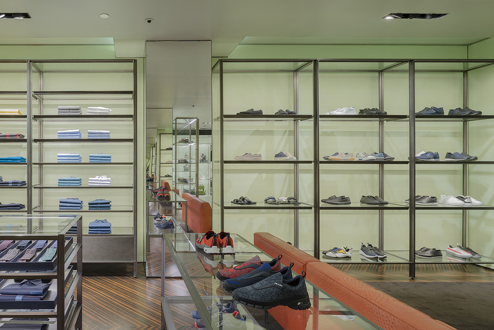 Prada store interior with shelves displaying various sneakers and folded apparel, between the shelves, facing mirrors featuring an infinity mirror effect.