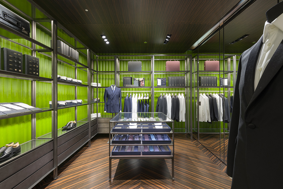 Luxury store interior with shelves showcasing men's suits, dress shirts, ties, and formal shoes.