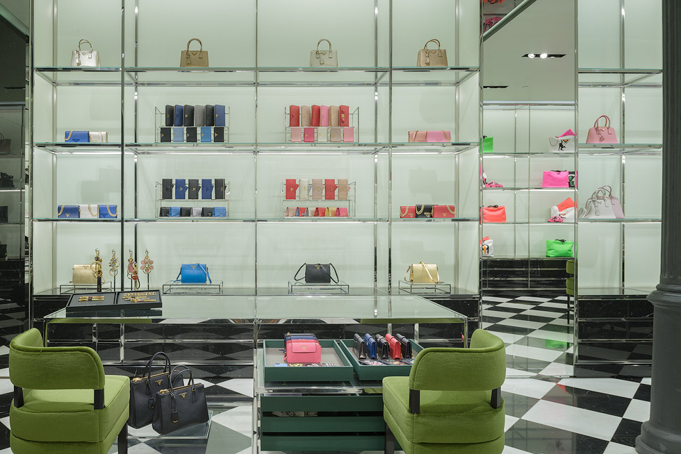 Luxury store interior with a display of colorful handbags and wallets, green chairs, and a checkered floor.