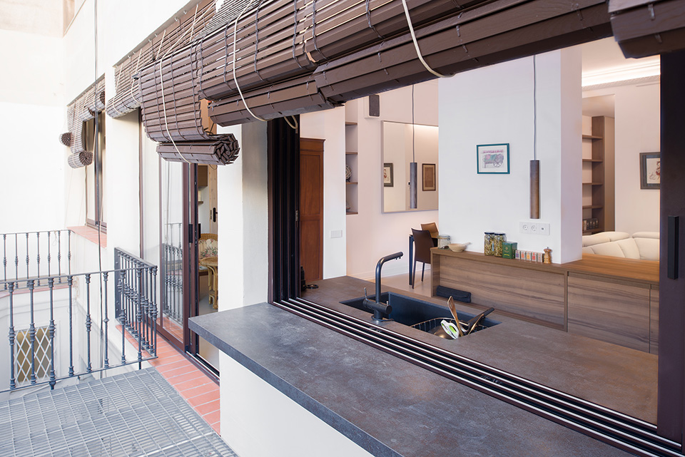 Modern kitchen with an open window bar to the outdoor terrace, featuring a sleek countertop and rolled-up blinds.