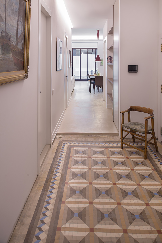 Hallway with geometric tiled floor, leading to a dining area with a red pendant lamp.