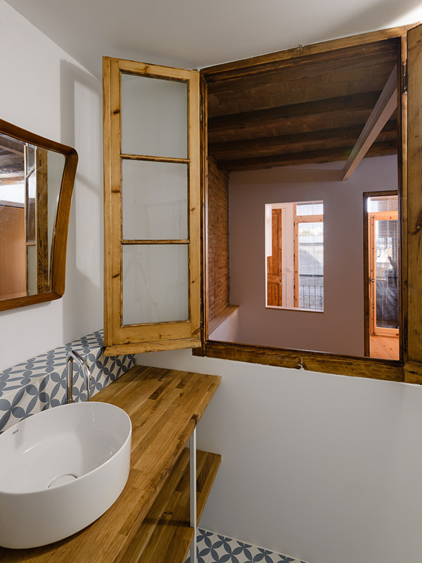 Bathroom with a wooden window opening into a bedroom, patterned tile backsplash, wooden countertop, and white basin sink.