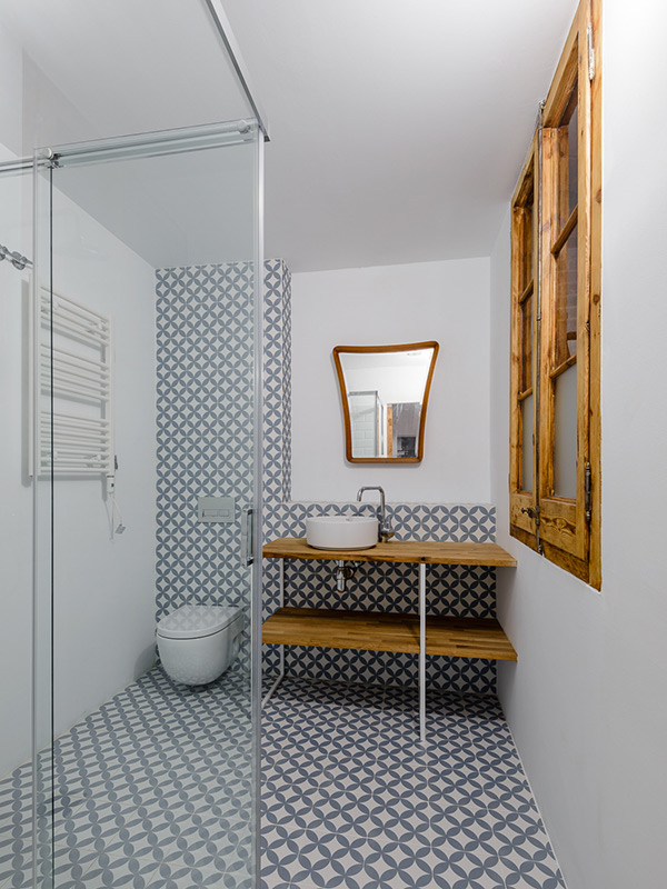 Bathroom with glass shower, patterned tilse, wooden countertop, white basin sink and vintage mid-century modern style wooden mirror.