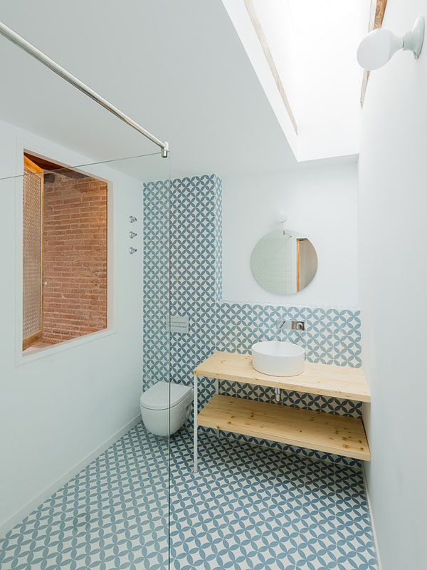 Bathroom with blue and white geometric tile design, round mirror, skylight, and a wooden vanity with a vessel sink.