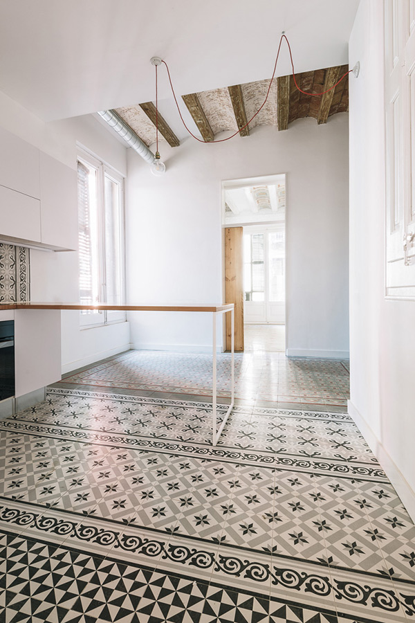 Bright kitchen with patterned floor tiles, exposed wooden beams, and a minimalist work table.