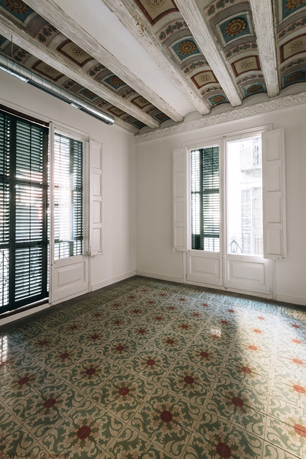 Room with patterned floor tiles, ornate beamed ceiling, and large windows with shutters.