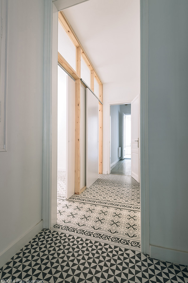 Hallway with patterned floor tiles and wooden frame elements leading to a bright room.