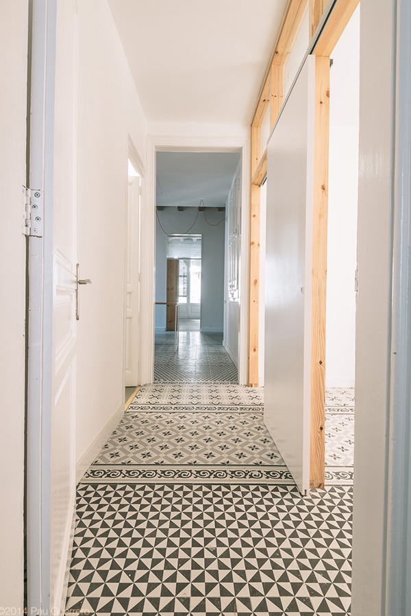 Hallway with patterned floor tiles and a wooden frame leading to a bright room.