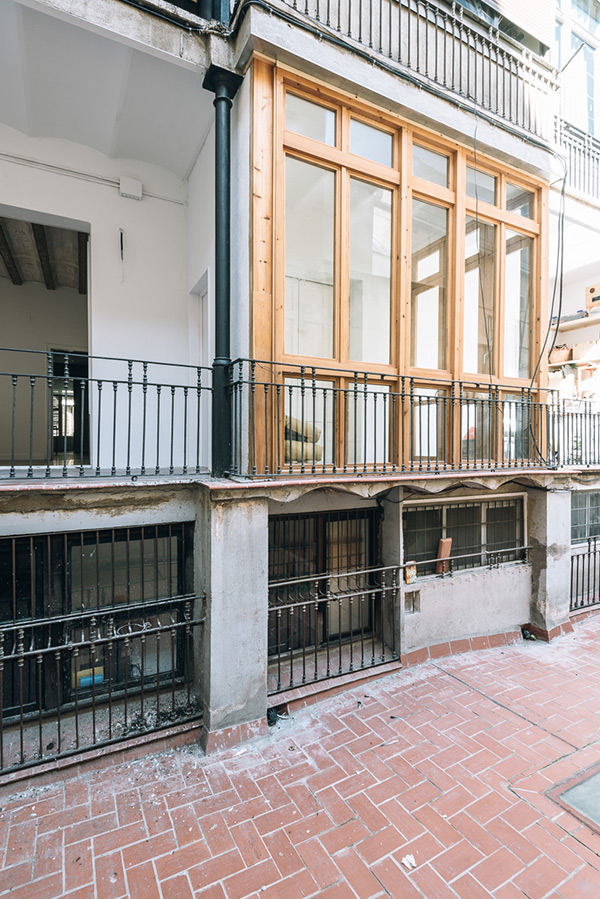 Renovated balcony with wooden frames and iron railings overlooking a brick patio.