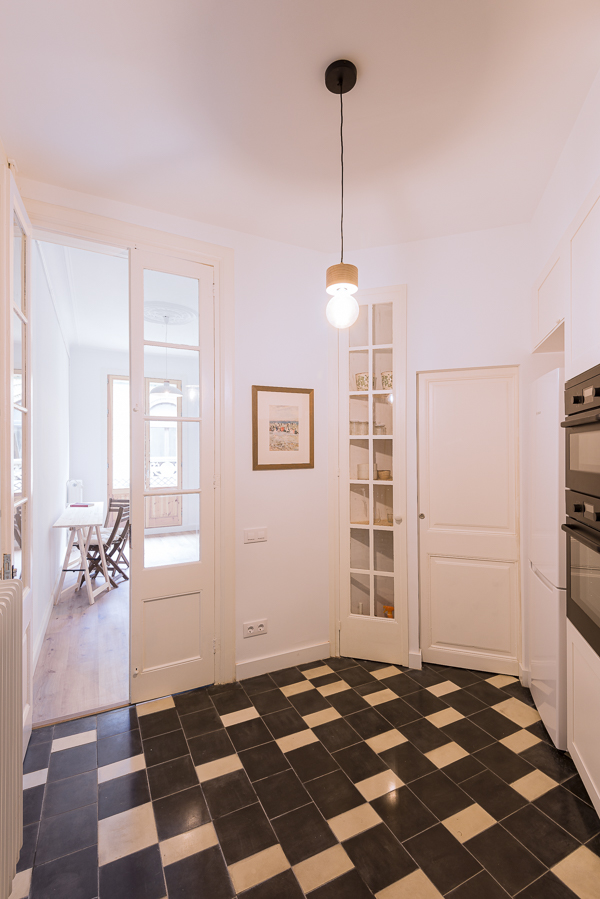 Bright kitchen with checkered floor tiles, white cabinetry, and glass-paneled doors leading to a room with a studio area.