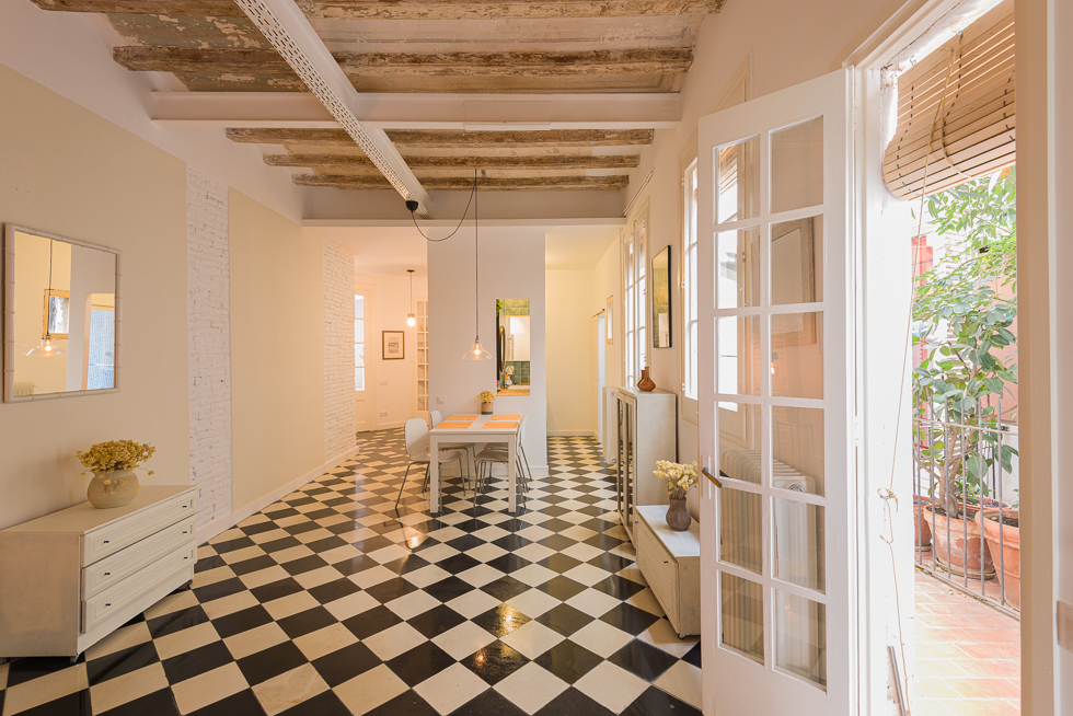 Spacious dining area with checkered floor tiles, exposed beams, and French doors opening to a patio area.