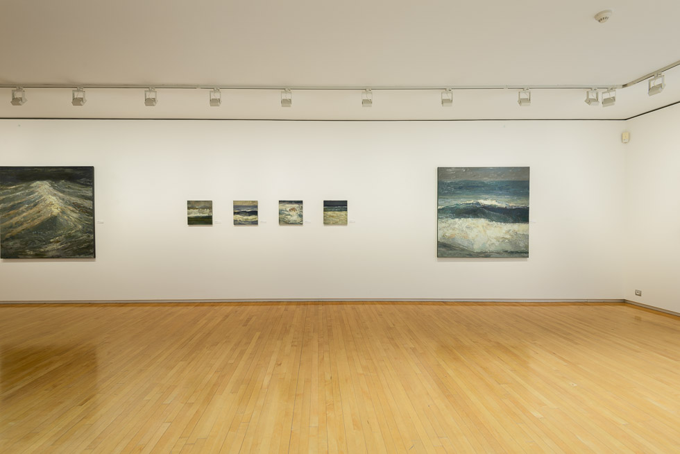 Art gallery with wooden floors and white walls, featuring a series of seascape paintings of different sizes displayed in a row.