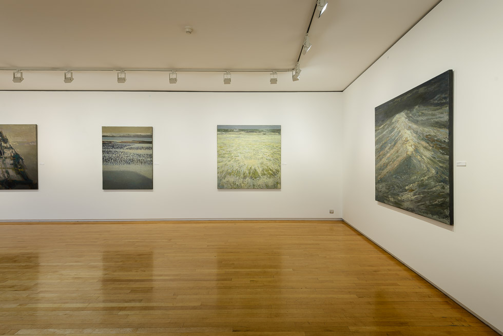 Close-up of seascape paintings in a gallery with wooden floors, white walls, and overhead track lighting.