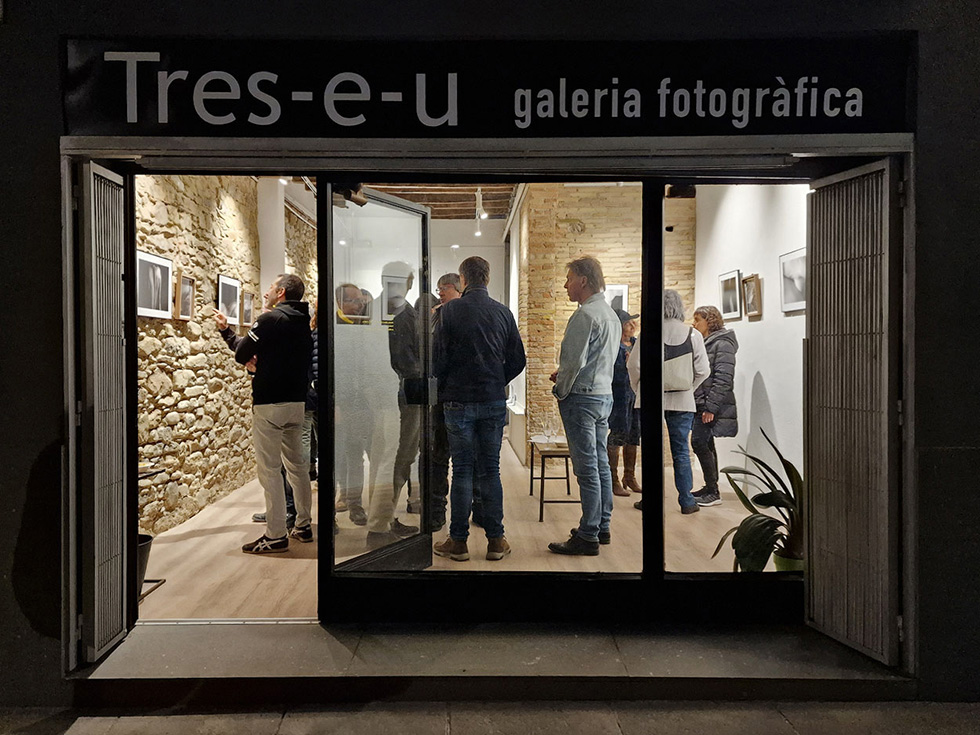 People observing photographs at the Tres-e-u photography gallery, as seen from the street through the gallery's main entrance.